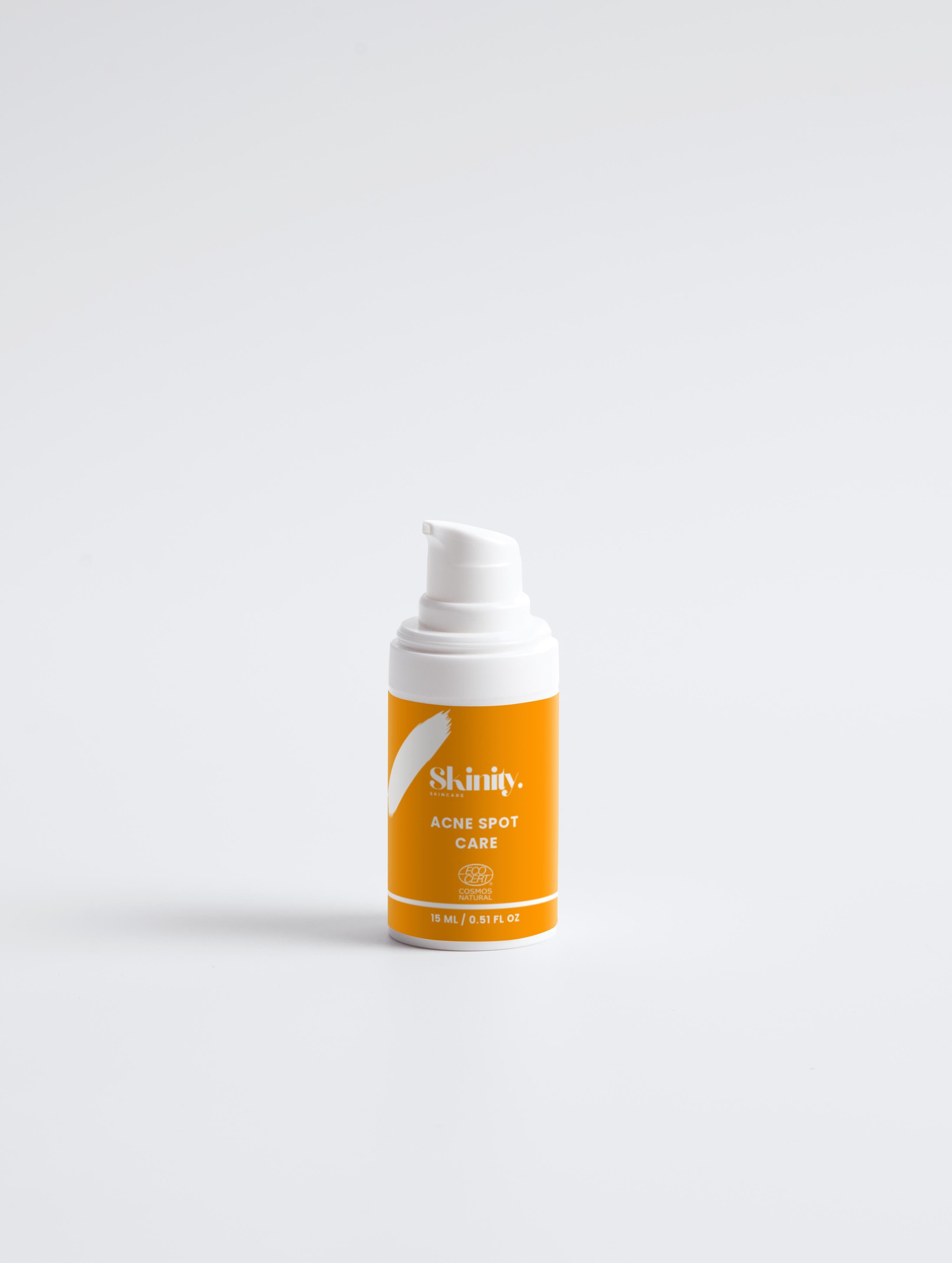 Acne Spot Care Serum For All Skin Types in a white and orange pump bottle on a minimal background.