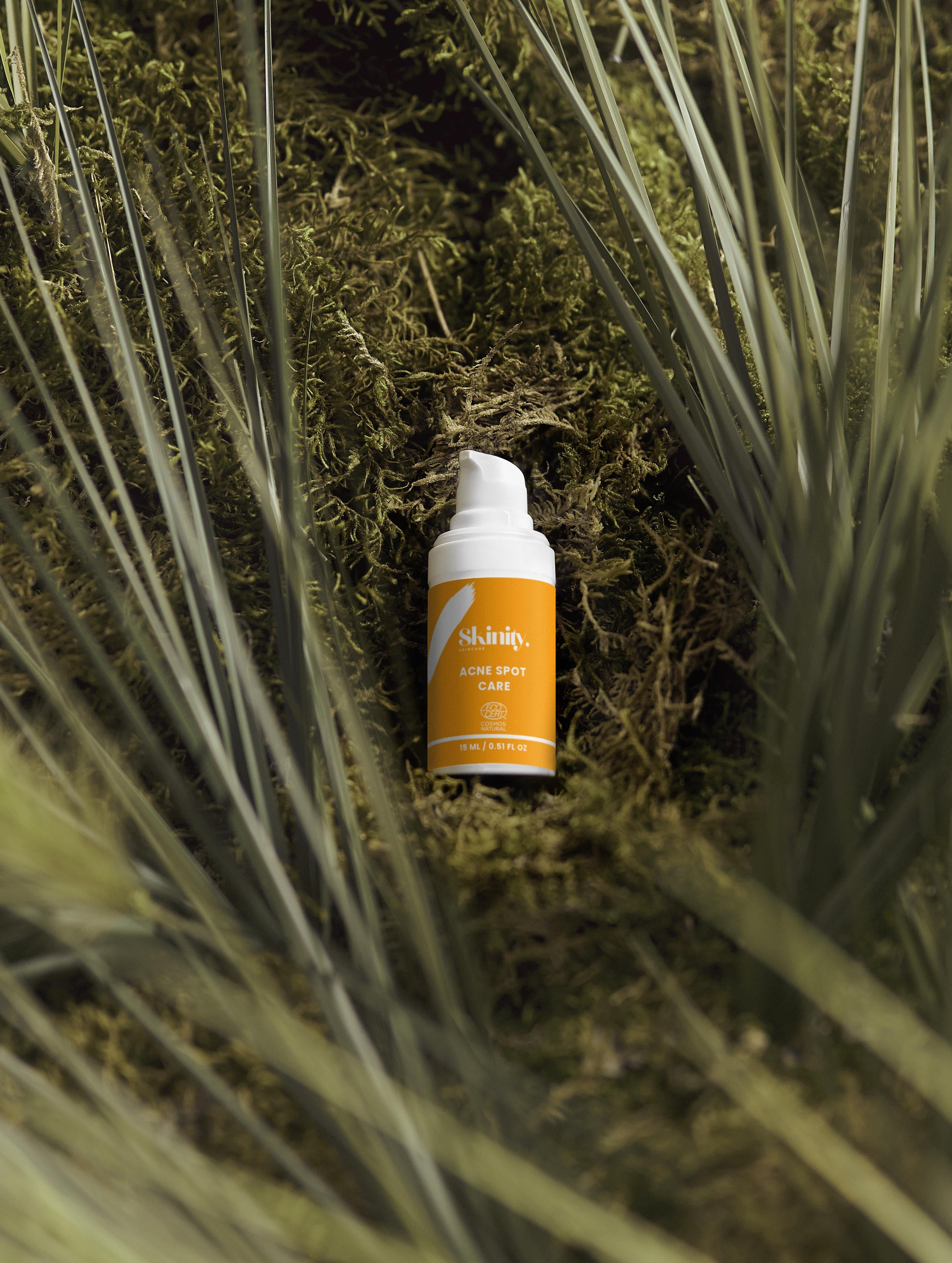 Acne Spot Care Serum for All Skin Types bottle surrounded by greenery, designed to reduce redness and blemishes.