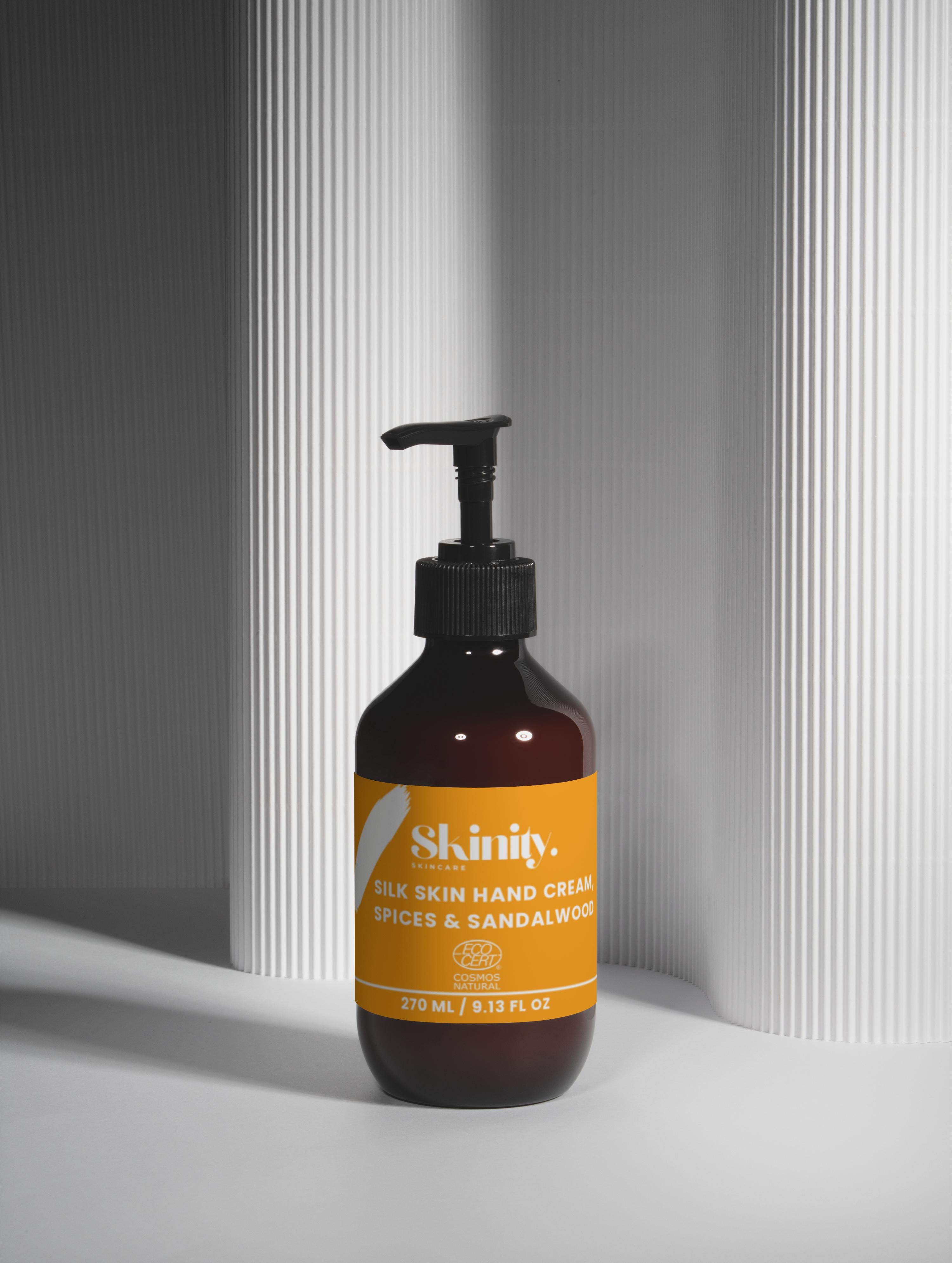 Silk Skin Hand Cream Spices and Sandalwood in a dark bottle with pump against a textured background.