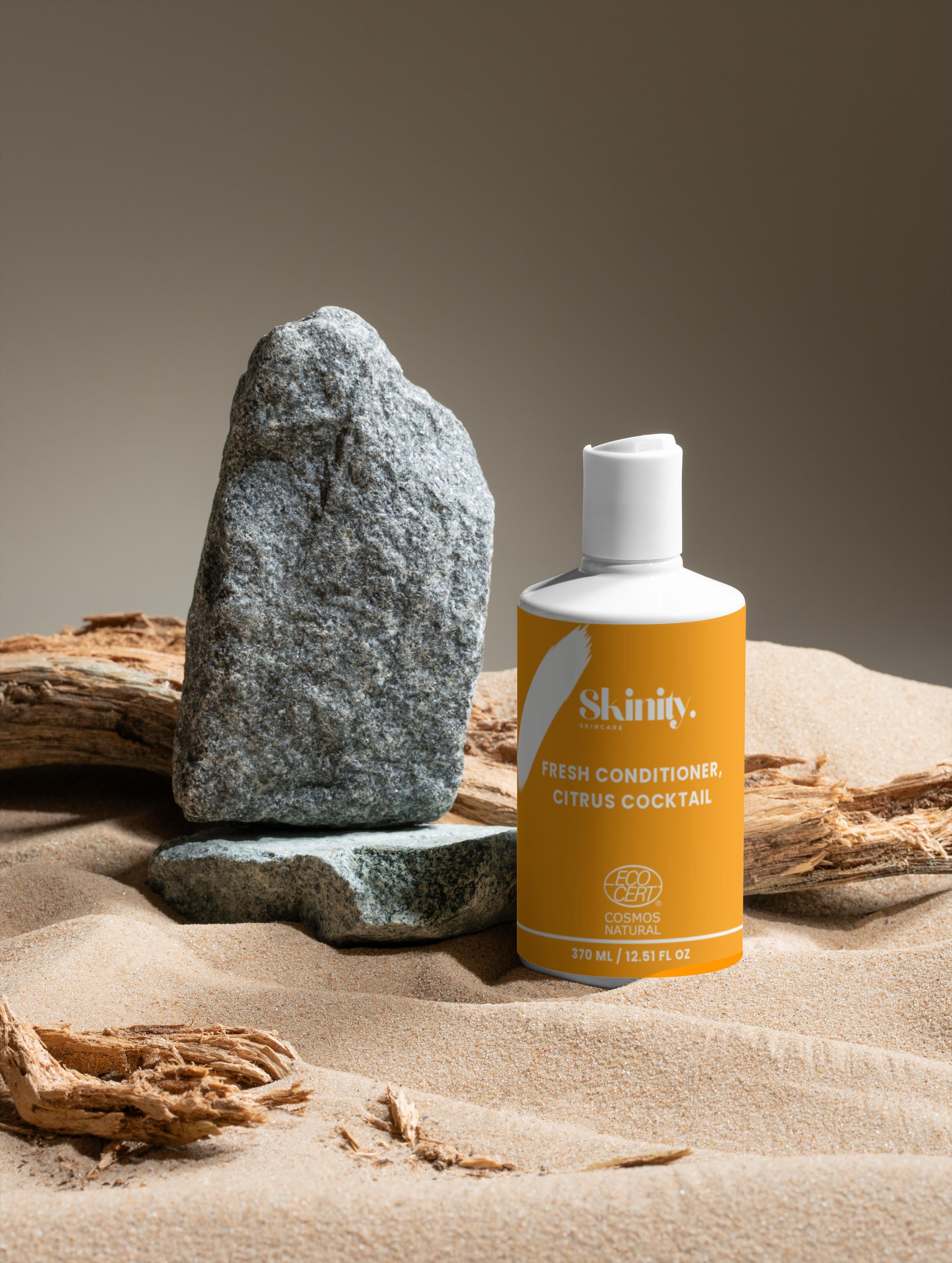 Fresh Conditioner Citrus Cocktail bottle positioned next to rocks and driftwood on sandy background.