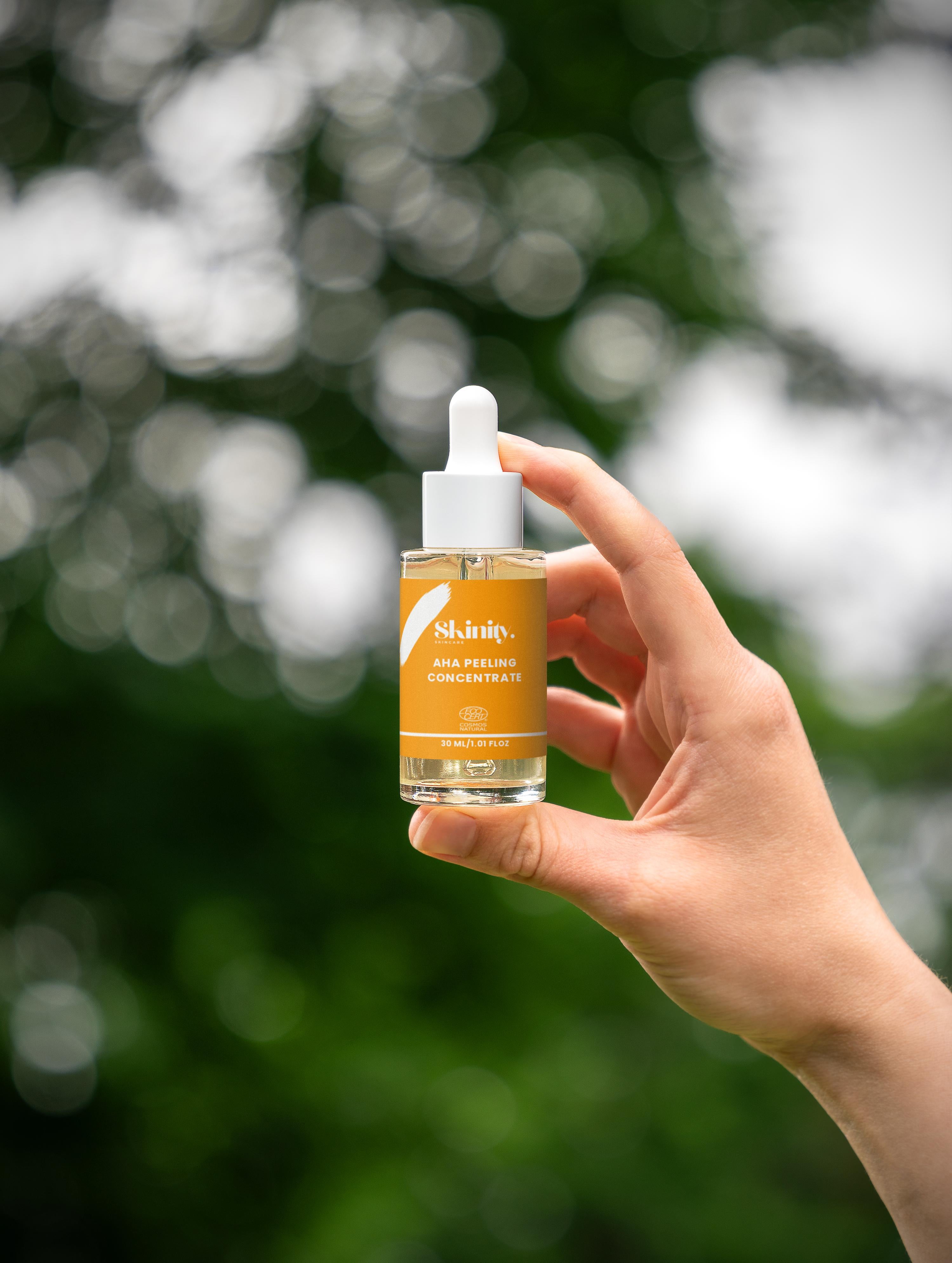 A person holding AHA Peeling Concentrate For Skin serum against a blurred green background.