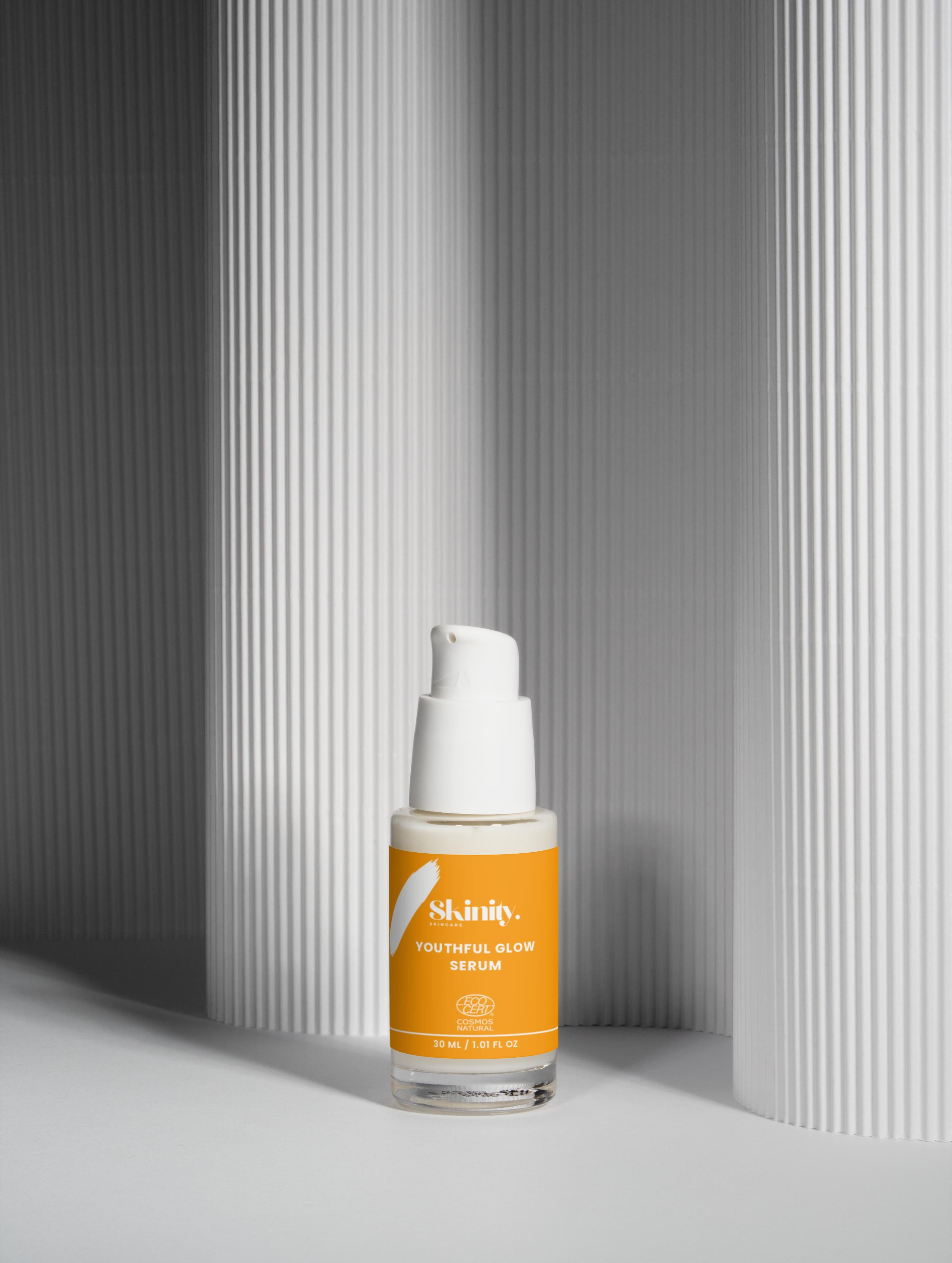Youthful Glow Serum For All Skin Types in a bottle with a sleek design and orange label against a textured background.