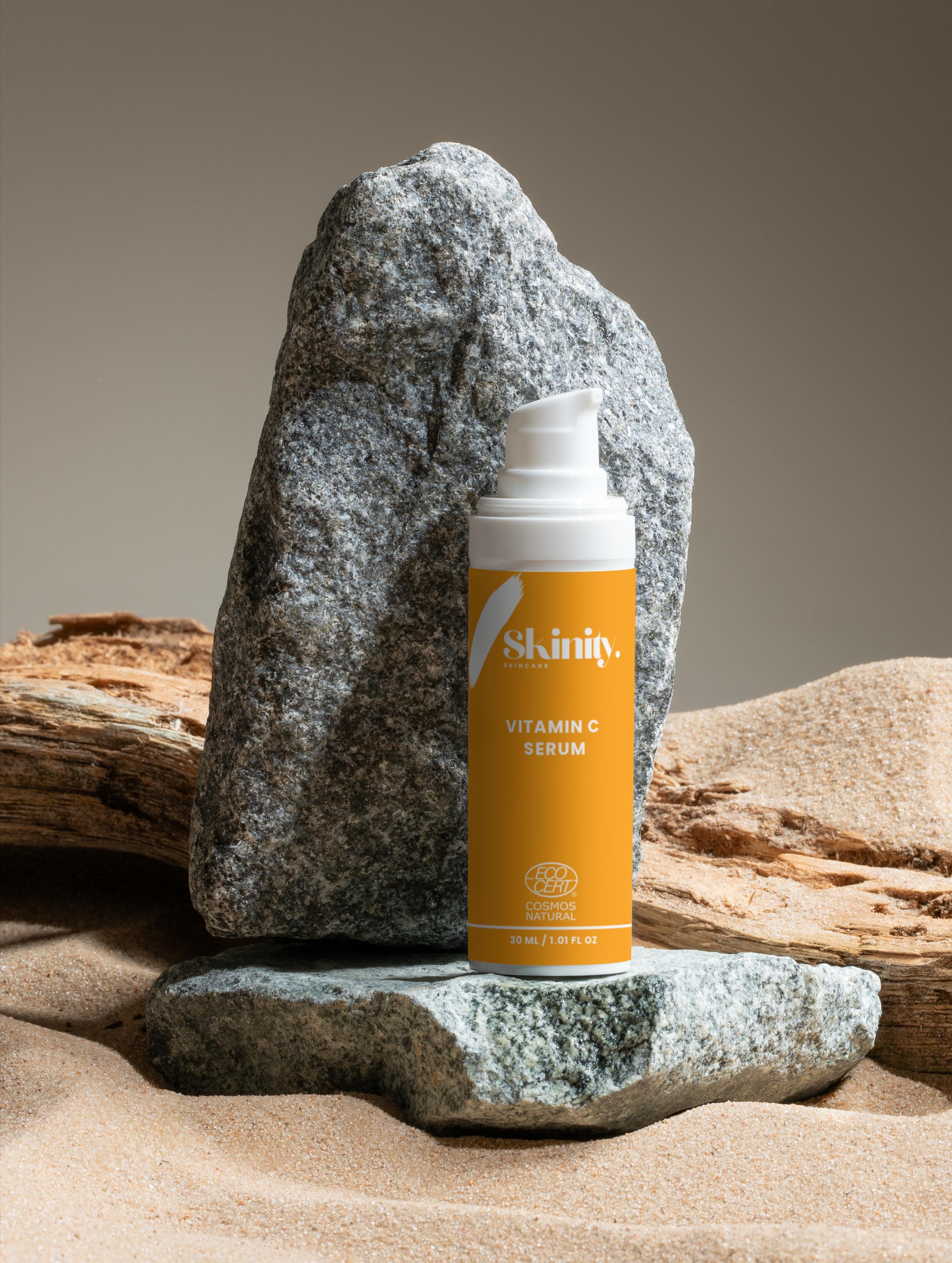 Vitamin C serum for all skin types placed on a stone in a sandy setting.