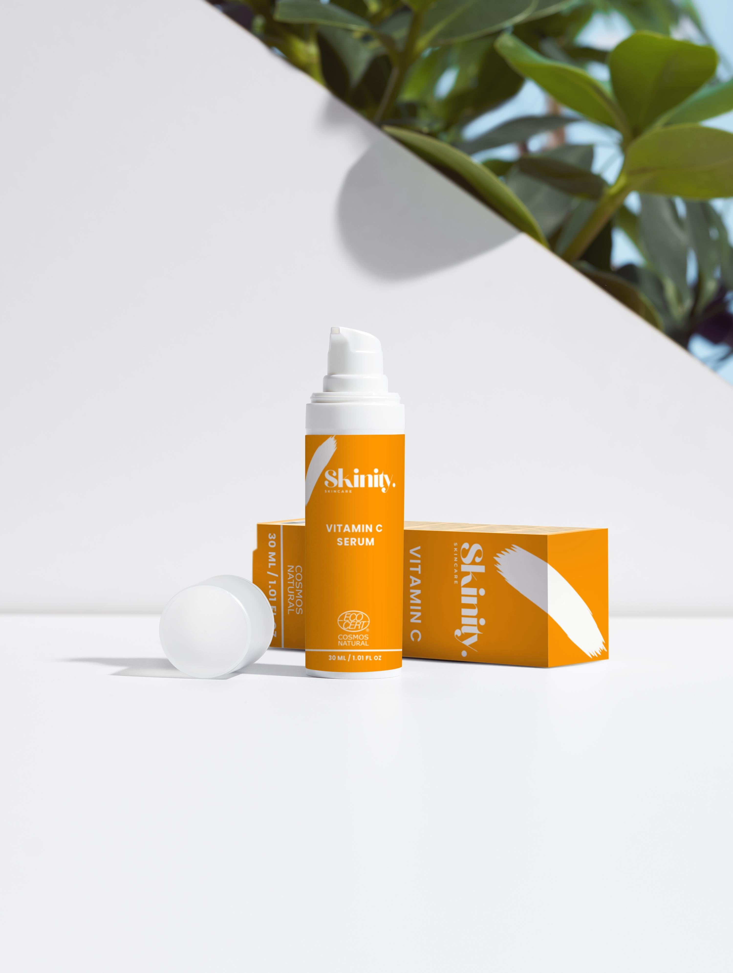 Vitamin C serum for all skin types in an elegant packaging on a clean surface with green leaves in the background.