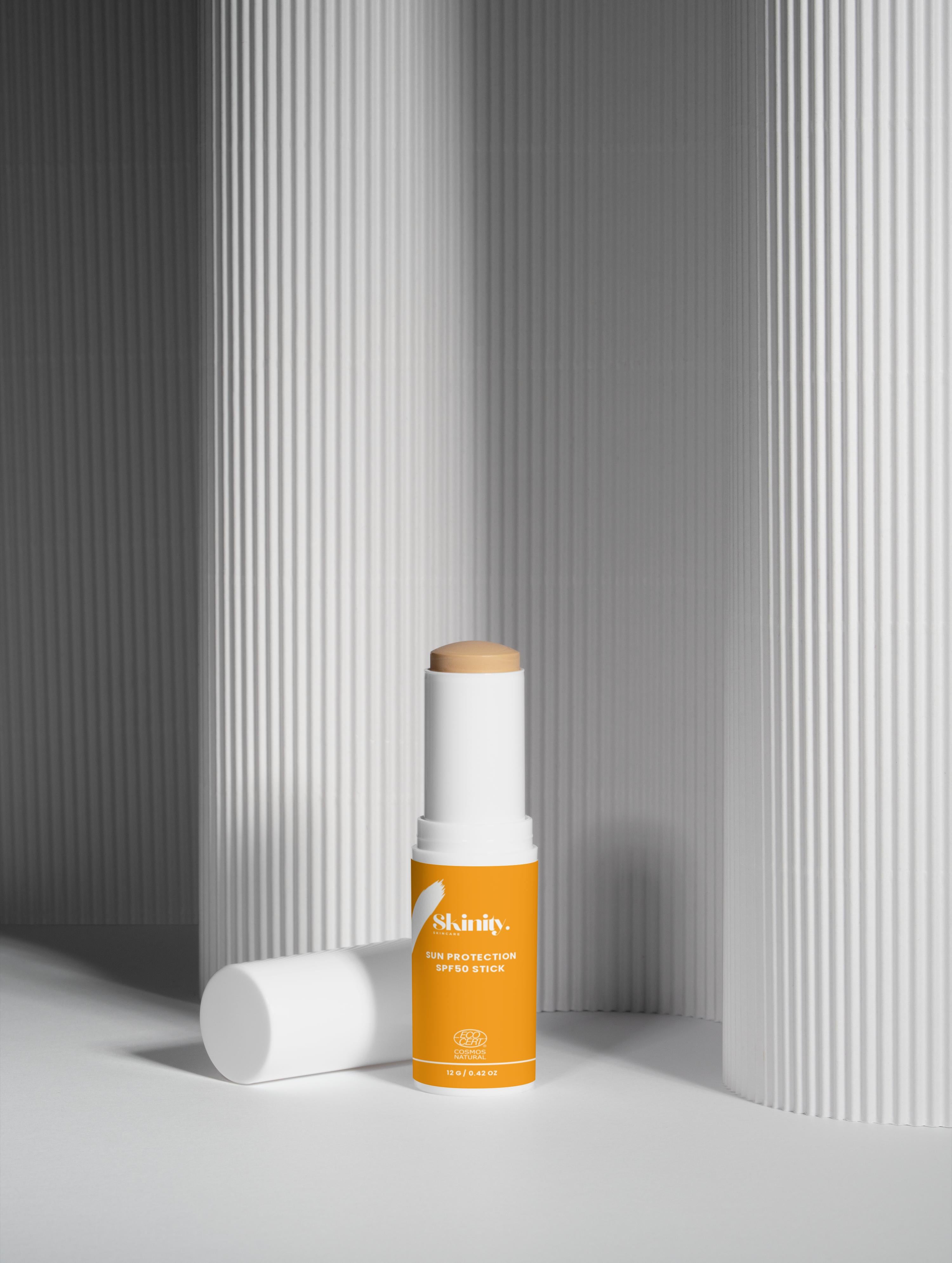 SPF 50 tinted sunscreen stick leaning against white ribbed columns for high-performance UV protection.