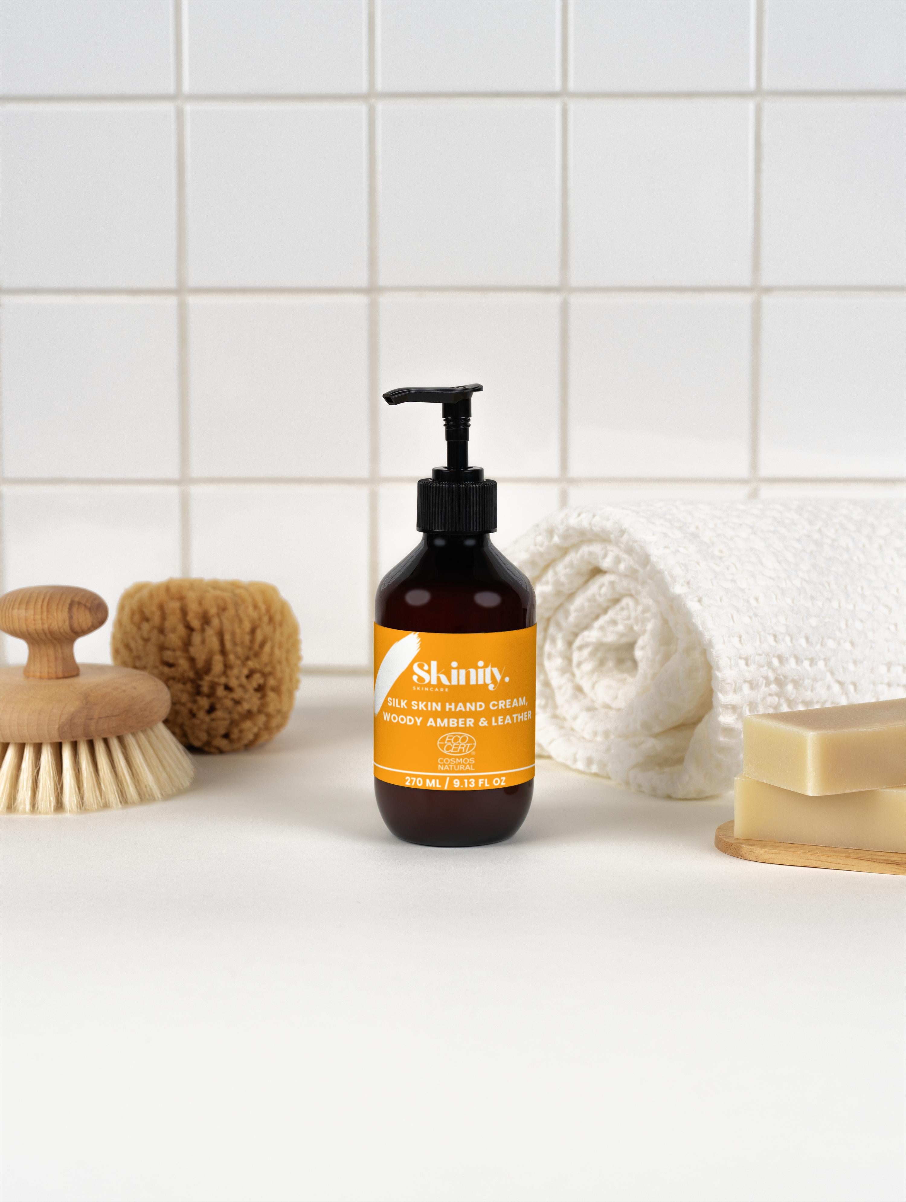 Silk Skin Hand Cream Woody Amber and Leather bottle with bath accessories on countertop
