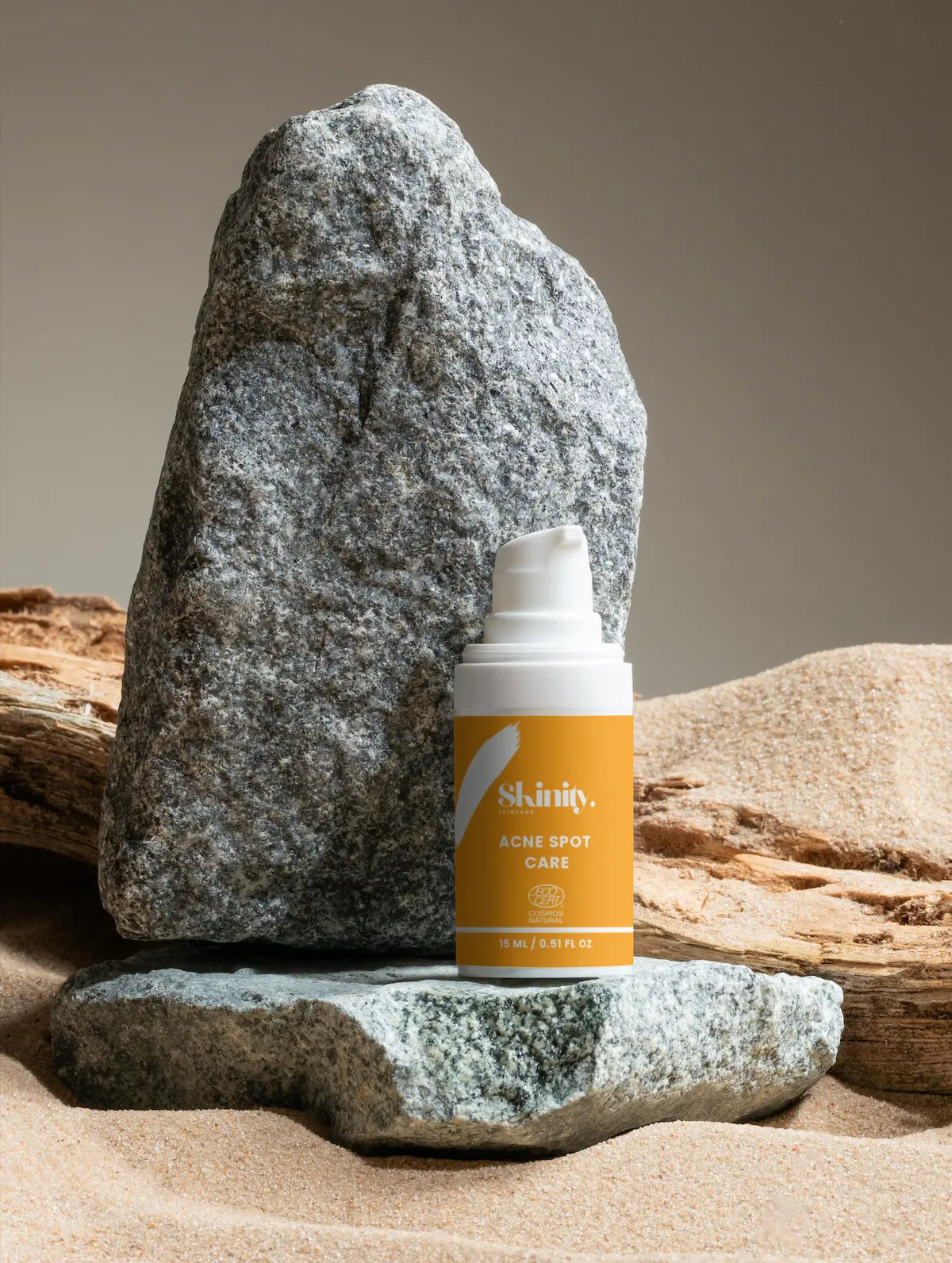 Skinity Acne Spot Care bottle displayed on a grey stone with a natural sand background.