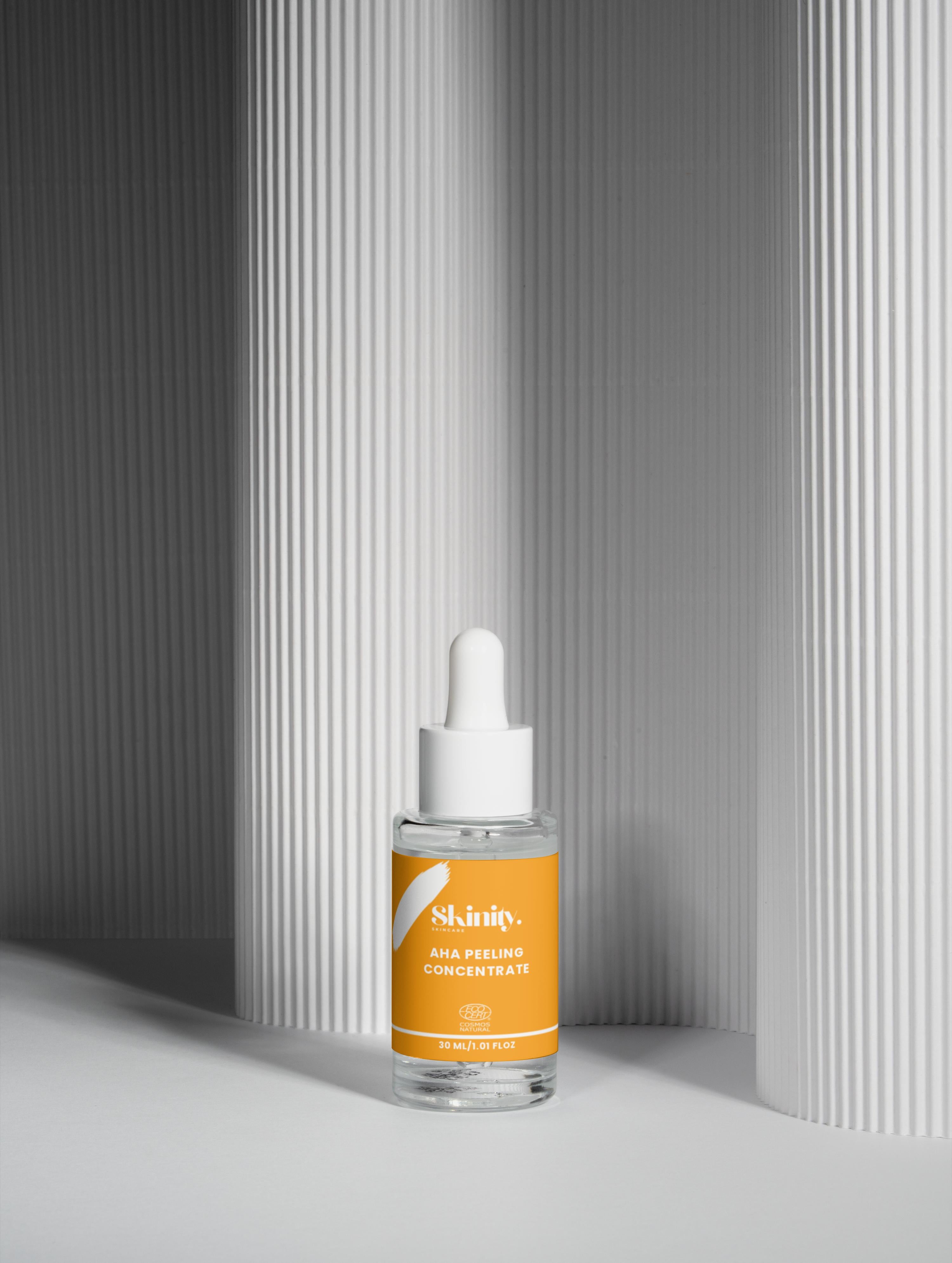 AHA Peeling Concentrate For Skin in a clear bottle with white dropper on a textured background.