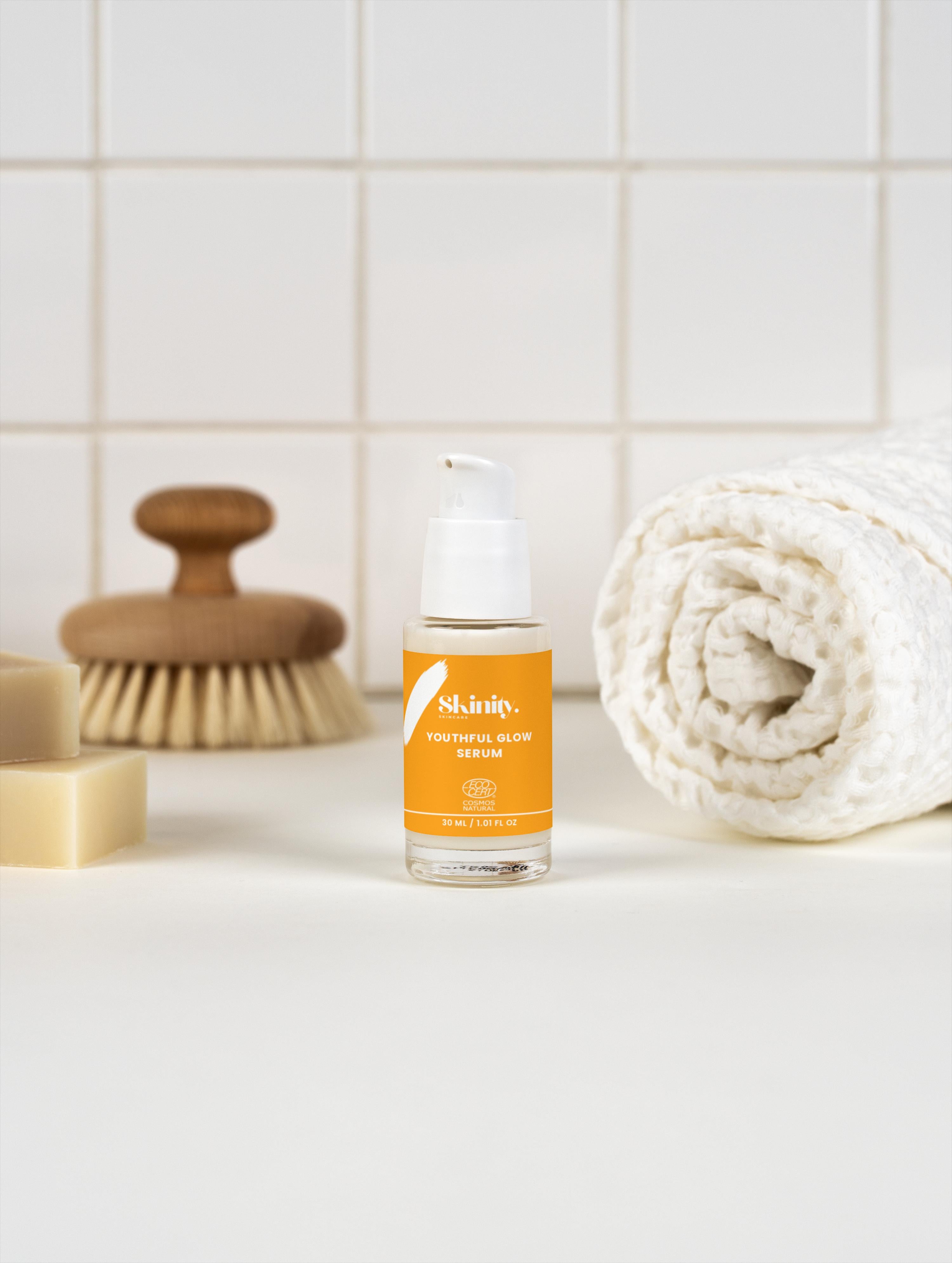 Youthful Glow Serum For All Skin Types on a countertop with a brush and rolled towel.